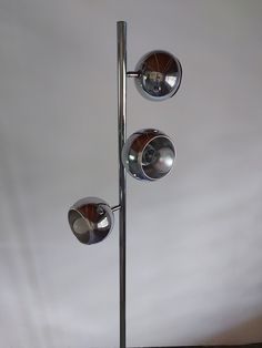 three lights that are on top of a metal pole in front of a white wall