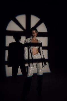 a woman standing next to a man in front of a window with shadows on it