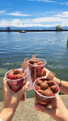 two people holding plastic cups with strawberries in them and forks sticking out of them