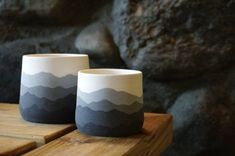 two cups sitting on top of a wooden table next to a large rock formation in the background