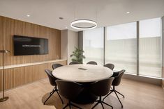 an office meeting room with a large round table and black chairs in front of a flat screen tv mounted on the wall