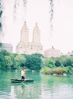 two people in a row boat on a river with tall buildings in the back ground