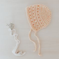 a crocheted hat next to a flower on a white surface