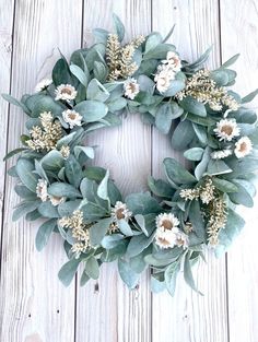 a wreath made out of eucalyptus leaves and white flowers on a wooden background with text overlay