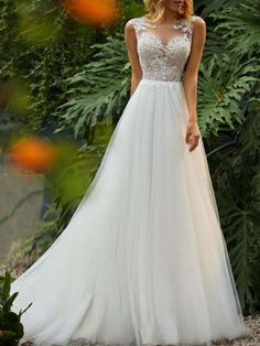 a woman in a white wedding dress standing on the ground near some trees and bushes