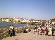 many people are walking on the sidewalk by the water