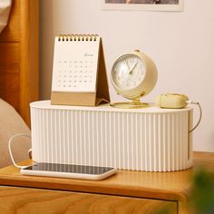 a desk with a clock, calendar and headphones on top of the table in front of a bed