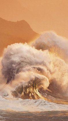 a large wave crashing into the ocean with mountains in the background