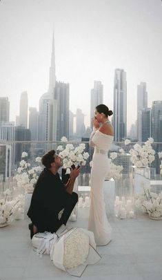 a man kneeling down next to a woman on top of a roof with white flowers