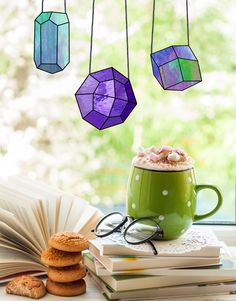 a cup of coffee and some cookies on a table next to an open book, with stained glass hanging from the ceiling