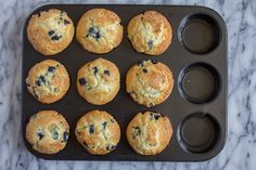 twelve blueberry muffins in a muffin tin on a marble countertop