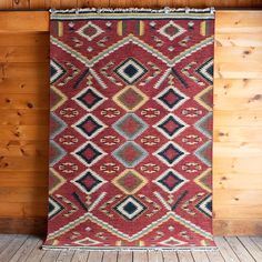 a red and black rug hanging on a wooden wall next to a wood paneled wall