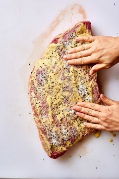 two hands on top of a raw piece of meat that is being prepared for cooking