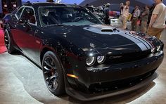 a black and red sports car on display at an auto show with people standing around