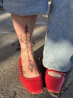 a woman's foot with a tattoo on her left leg and red shoes in the foreground