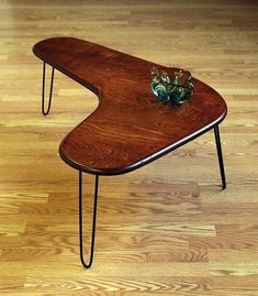 a wooden table with hairpin legs and a glass vase on the top, sitting on a hard wood floor