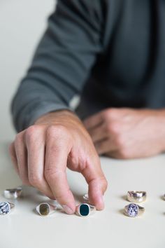 Man picking up a silver bloodstone signet ring next to tigers eye and pinolith signet rings and mens silver wedding bands Timeless Sterling Silver Signet Ring With Gemstone, Vintage Sterling Silver Signet Ring With Gemstone, Heirloom Style Open Signet Ring With Gemstone, Artisan Sterling Silver Engraved Hallmarked Ring, Classic Untreated Sterling Silver Rings, Unique Oval Sterling Silver Signet Ring, Untreated Sterling Silver Rings - Fine Jewelry, Sterling Silver Signet Ring With Gemstone For Gift, Sterling Silver Gemstone Signet Ring Fine Jewelry