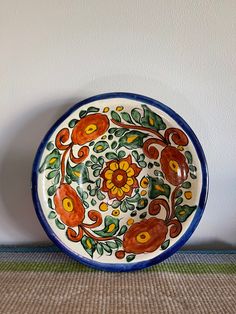 a decorative plate with flowers painted on the front and sides, sitting against a white wall