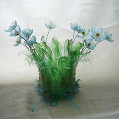 a green vase filled with blue flowers sitting on top of a white cloth covered table