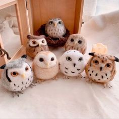 several stuffed owls sitting in front of a mirror on a white bed sheet with a basket behind them