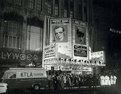 an old black and white photo of people standing in front of a movie theater at night