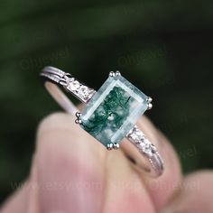 a person holding a ring with a green and white stone in it's middle