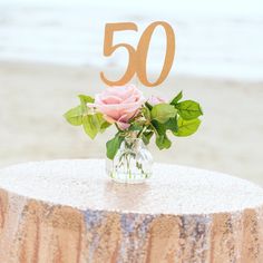 a small vase filled with pink roses sitting on top of a table next to the ocean