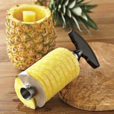 a pineapple peeler next to a knife on top of a wooden cutting board