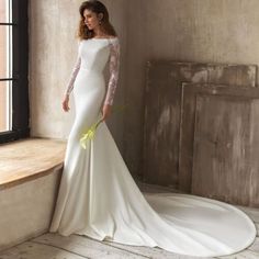 a woman in a white wedding dress leaning against a window sill with her hands on her hips