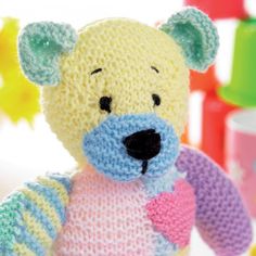 a crocheted teddy bear with a heart on it's chest sitting in front of toys