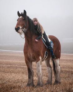 a woman riding on the back of a brown and white horse in an open field