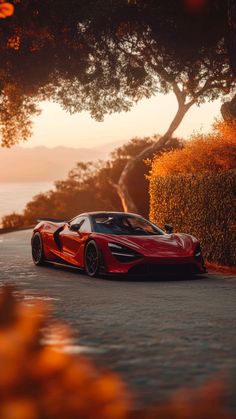 a red sports car parked on the side of a road next to bushes and trees