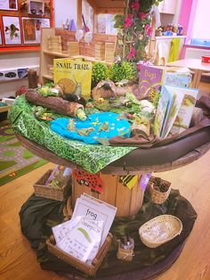 there is a table with many books on it in the middle of a room filled with children's toys