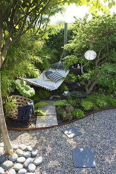 a garden with rocks, gravel and trees in the foreground is a hammock hanging from a tree