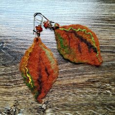 two orange and green leaf shaped earrings on a wooden surface with beads hanging from them