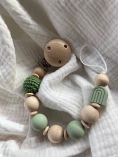 a wooden beaded necklace with green beads and a button on the clasp is laying on a white blanket