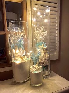 three glass vases with flowers and lights in them on a table next to a window