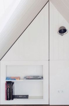 a book shelf in the corner of a room under a slanted roof with white walls