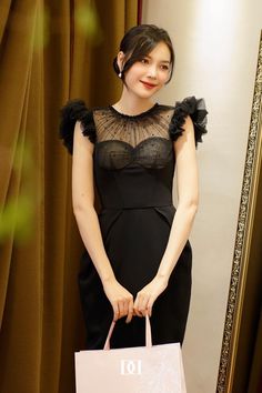 a woman in a black dress holding a pink shopping bag and posing for the camera