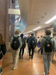 many people are walking down the hallway in an office building with backpacks on their backs