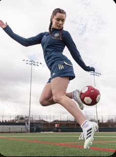 a woman kicking a soccer ball on top of a field