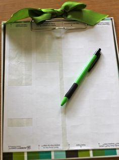 a clipboard with a notepad, pen and green bow on it sitting on a table