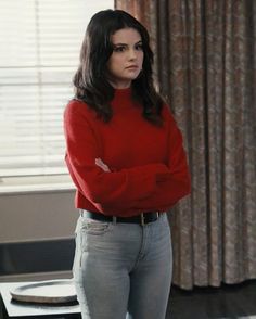 a woman in a red sweater and jeans stands with her arms crossed