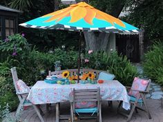 an outdoor table and chairs set up for a meal with sunflowers on the table