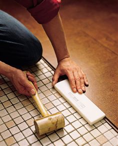 a person kneeling down on the floor with a brush in their hand next to a tile surface