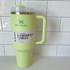 a green travel mug sitting on top of a counter next to a white tile wall