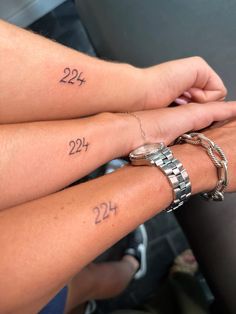 two people holding hands with numbers on their wrists and tattoos on their arms, while the other hand holds another person's wrist