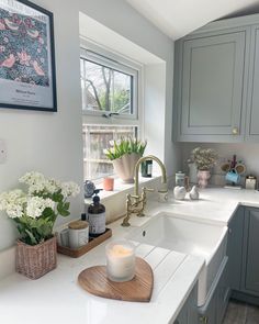 a kitchen with gray cabinets, white counter tops and flowers in vases on the sink