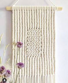 a white wall hanging with purple flowers in front of it on a wooden hanger