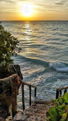 the sun is setting over the ocean and there are steps leading down to the water